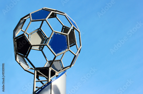 Tablou pe pânză symbolic metal soccer ball on socle against blue sky background