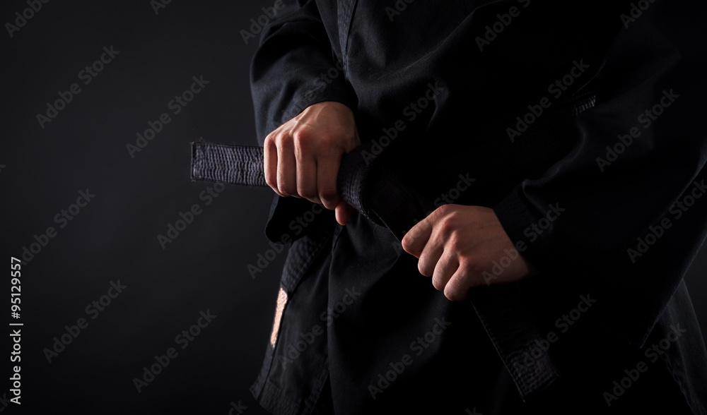 Closeup of male karate fighter tying the knot to his black belt