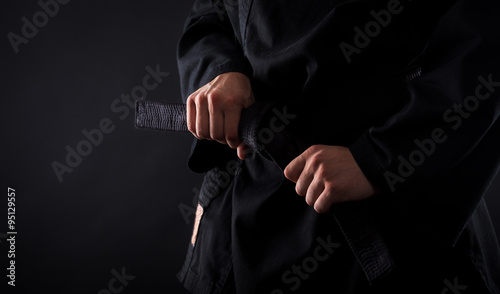 Closeup of male karate fighter tying the knot to his black belt