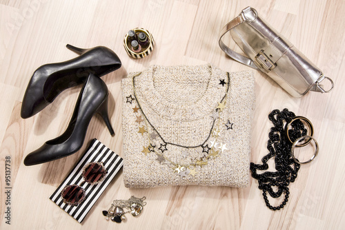Winter sweater and accessories arranged on the floor. Woman black with gold and silver accessories, high heels, bracelets, necklace and nail polish.