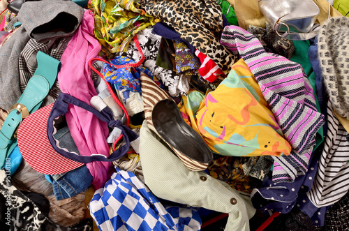 Close up on a big pile of clothes and accessories thrown on the ground. Untidy cluttered wardrobe with colorful clothes and accessories.