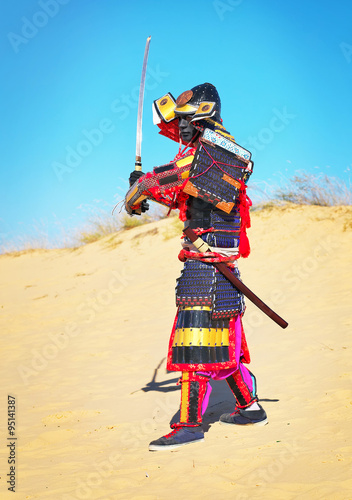 Man in samurai costume with sword running on the sand. 