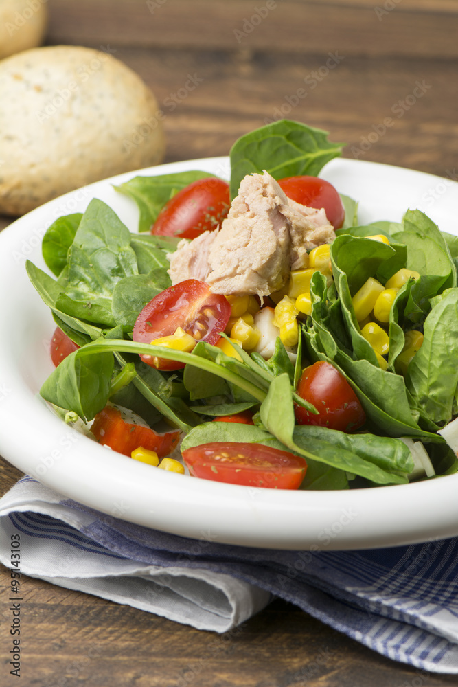Fresh spinach salad with tuna and corn, small pieces of cherry tomatoes in white plate Fresh spinach salad with tuna and corn, small pieces of cherry tomatoes in white plate