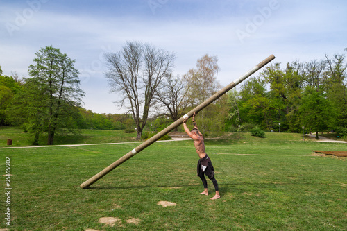 Young athlete man climbing the rope tied to metal construction as part of crossfit training.