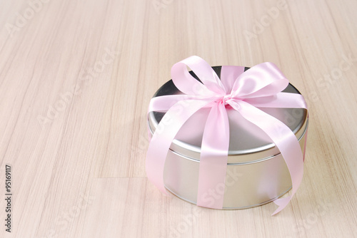 Gift in round tin box with pink ribbon background 