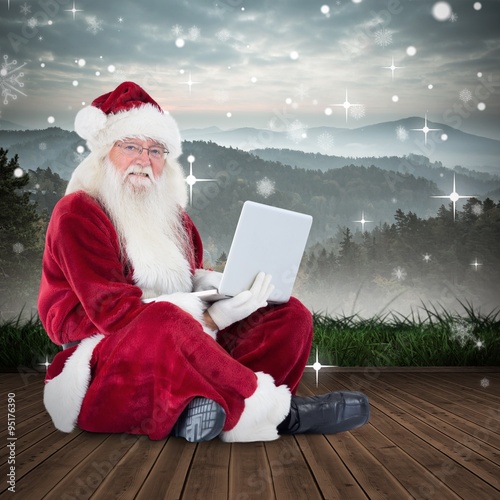 Composite image of santa sits and uses a laptop photo