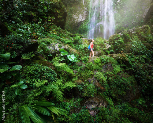 Young backpacker traveling along jungles, on background waterfal