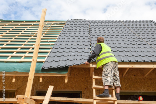 Roofer worker installing a metal tile on a new wooden house