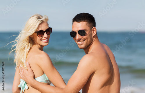 happy couple in swimwear sitting on summer beach