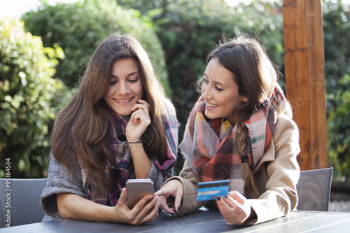 Two young friends shopping online with a credit card and a phone