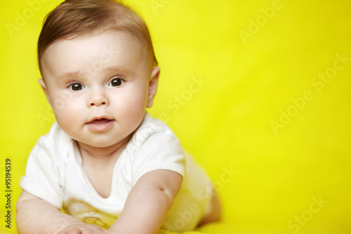 Surprised baby boy on his stomach looking to camera on yellow background. Cute infant kid over bright background.