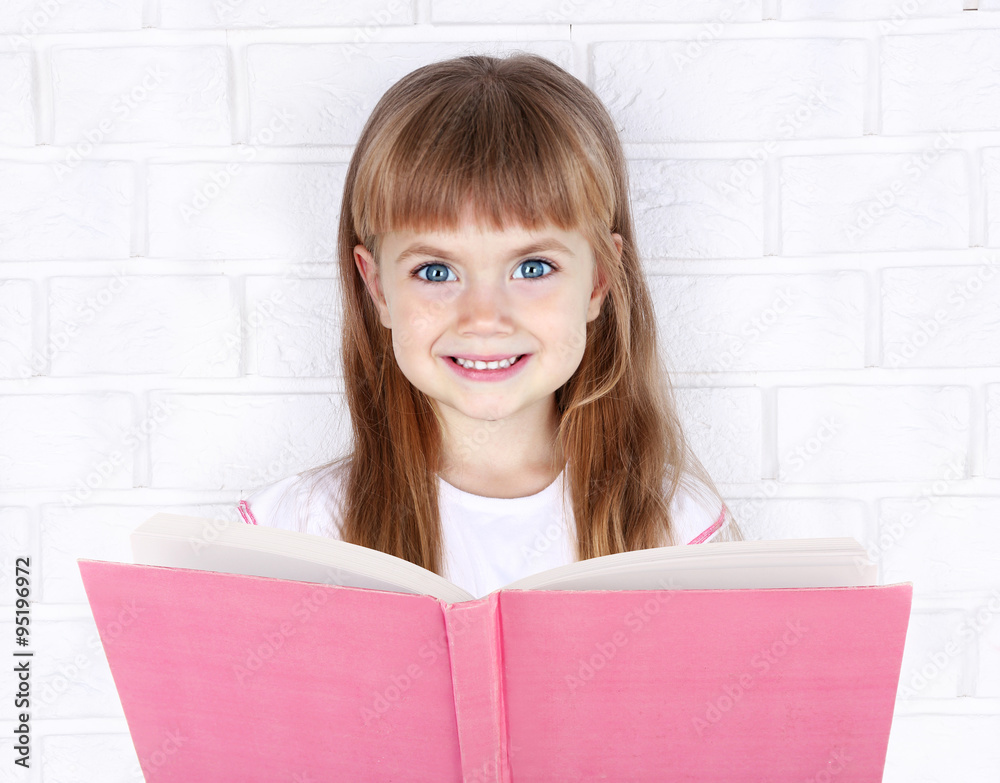 Beautiful little girl with book on wall background Beautiful little girl with book on wall background