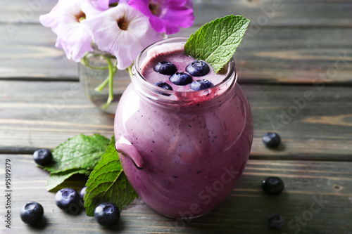 Glass jar of blueberry smoothie on wooden table, closeup