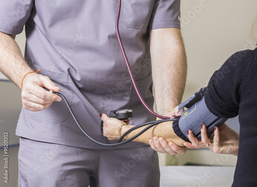 bearded doctor wearing glasses checks the patient's blood pressure and pulse