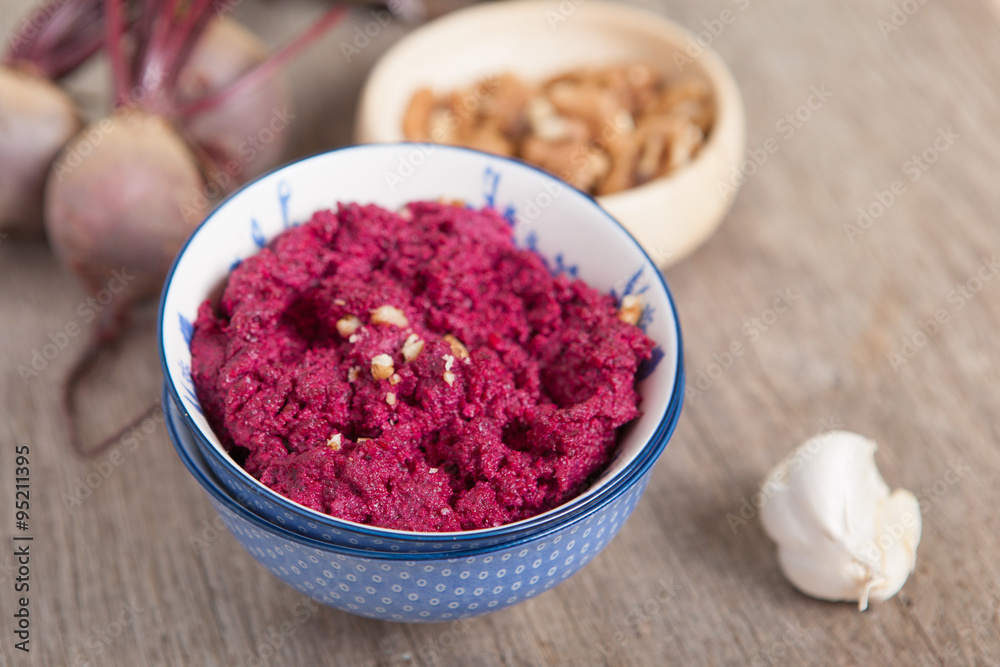 Beetroot pesto in a white bowl on a wooden table with garlic beetroot and rice cakes on the back, selective focus Beetroot pesto in a white bowl on a wooden table with garlic beetroot and rice cakes on the back, selective focus