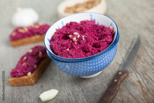 Beetroot pesto in a blue bowl on a wooden table with garlic beetroot and almond bread on the back  selective focus