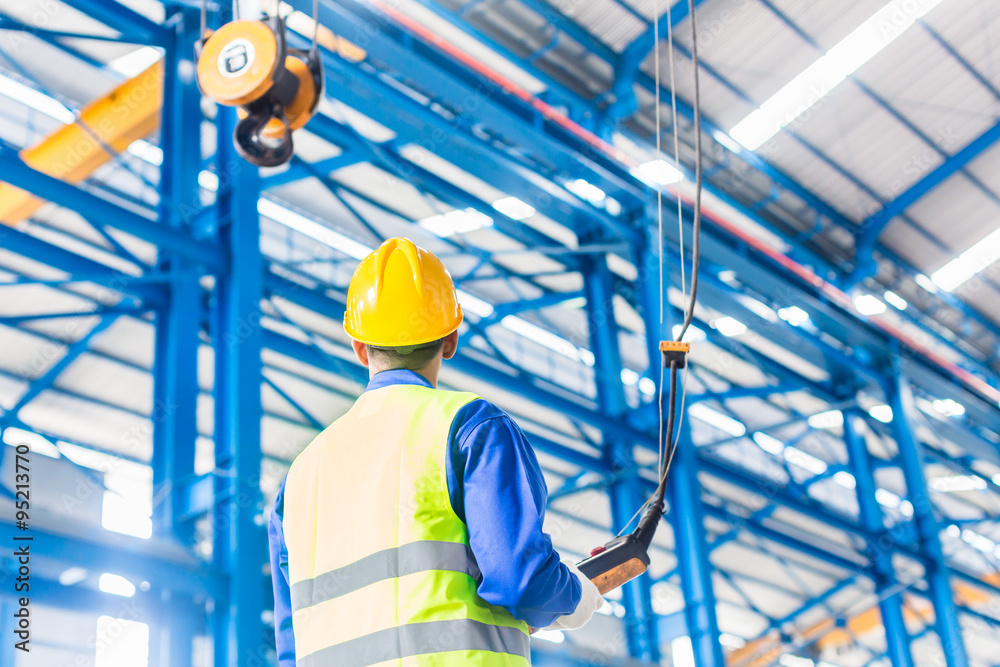 Worker in factory controlling crane with remote