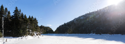 frozen lake under the winter sun in the middle of a forest of pins photo