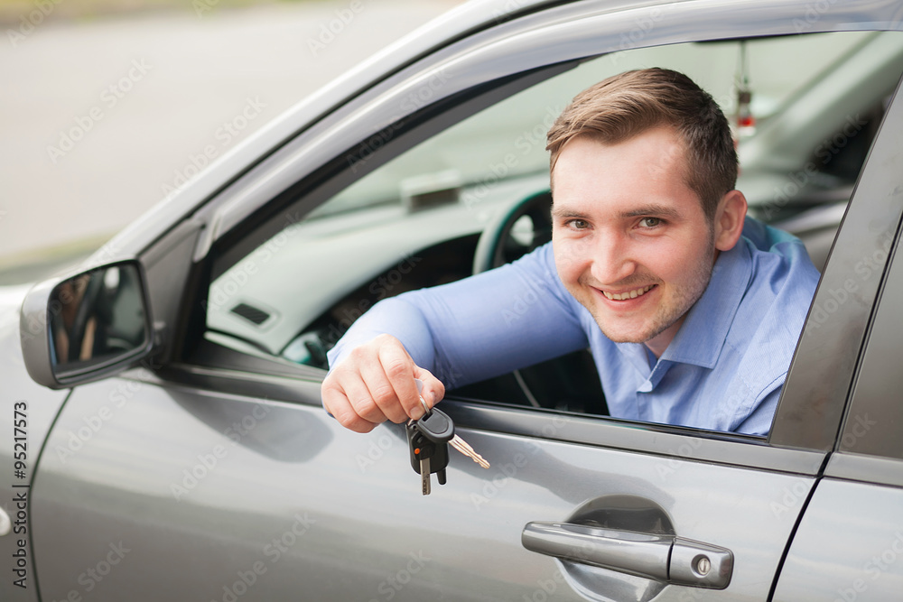 Young man sitting inside new car with keys. Smiling