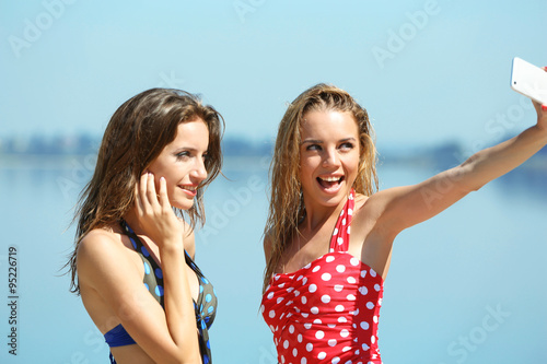 Two young girls making selfie on beach at summertime