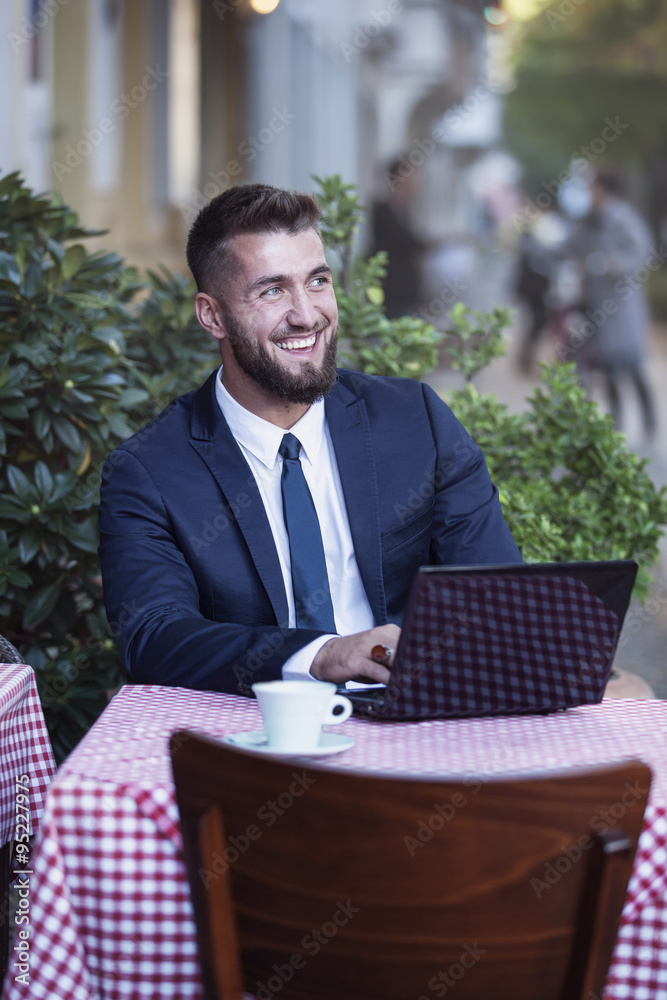 Glücklicher Geschäftsmann mit Laptop trinkt einen Kaffee im Strassencafe Glücklicher Geschäftsmann mit Laptop trinkt einen Kaffee im Strassencafe