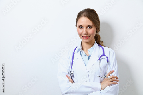Friendly smiling young female doctor  standing near wall
