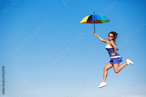 Young girl with umbrella jumping in the sky