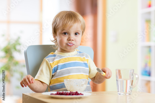 Child little boy eating food with spoon in nursery