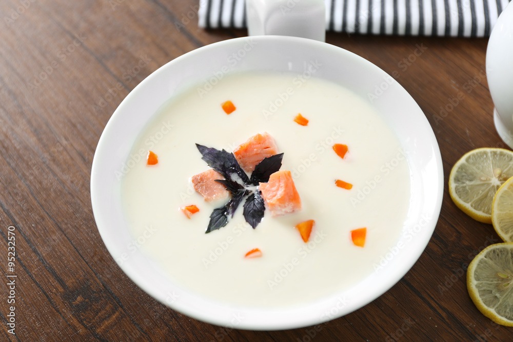 Delicious salmon cream soup in white plate on wooden table, close up Delicious salmon cream soup in white plate on wooden table, close up