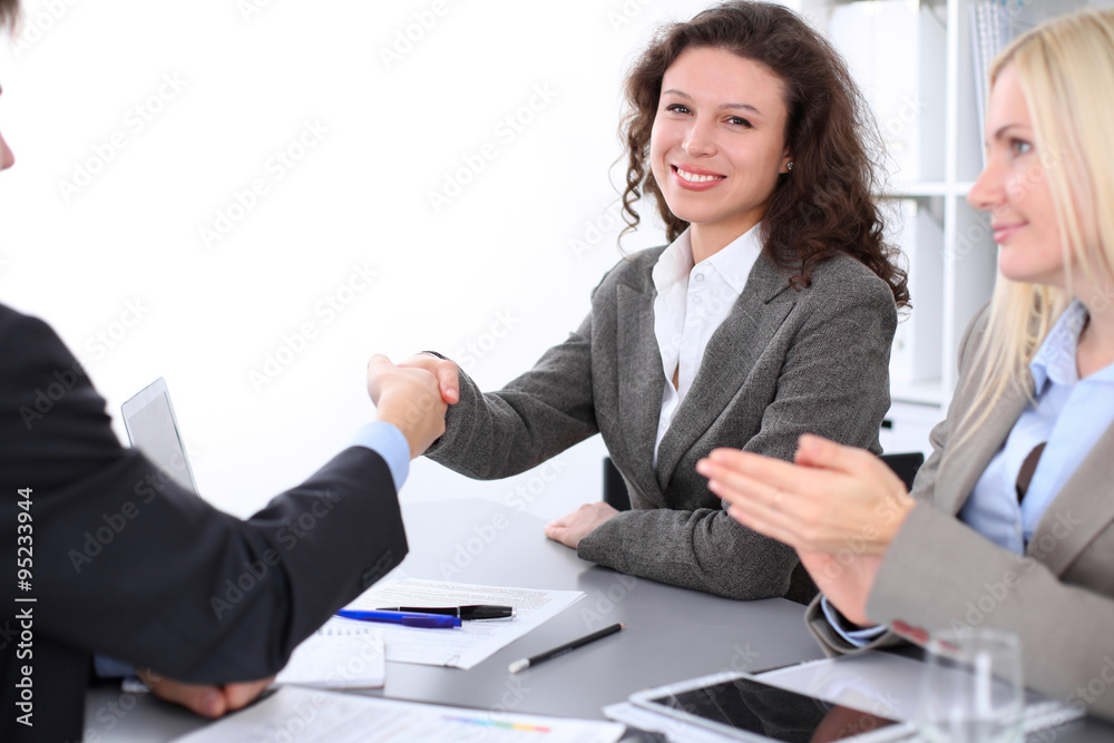 A group of business people at a meeting on the background of office. Focus on a beautiful brunette shaking hands A group of business people at a meeting on the background of office. Focus on a beautiful brunette shaking hands