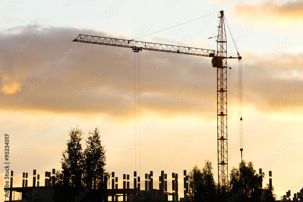 Silhouette of crane and building under construction in evening 
