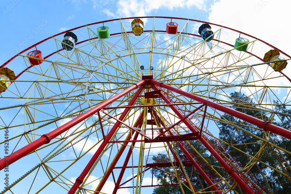 Half of colorful Ferris wheel and tops of trees and blue sky 