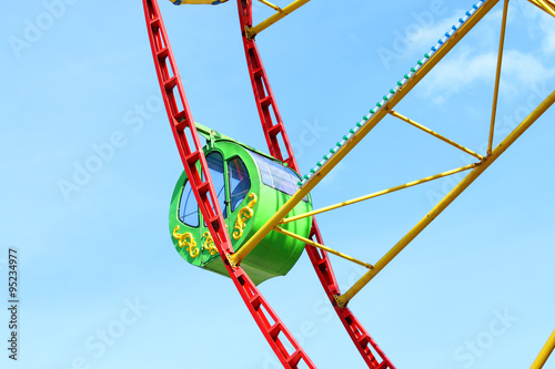 Green cabin of colorful Ferris wheel and blue sky with clouds at