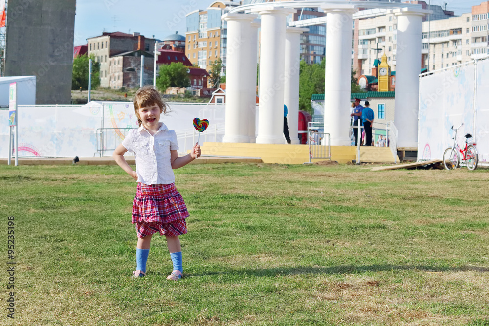 Happy little girl in skirt holds lollipop on grass outdoor 