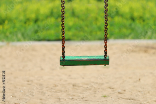 Green woioden swing on chain on playground at summer day