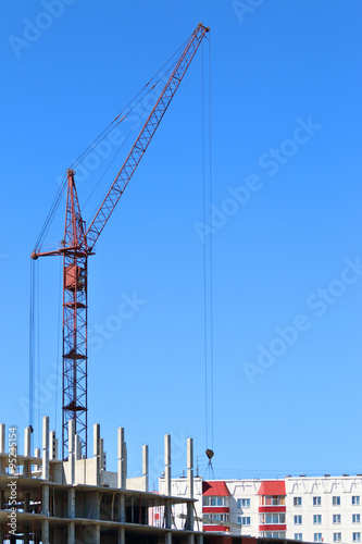 Red crane and part of building under construction at sunny day