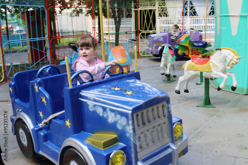 Little beautiful girl rides in car of carousel in amusement park