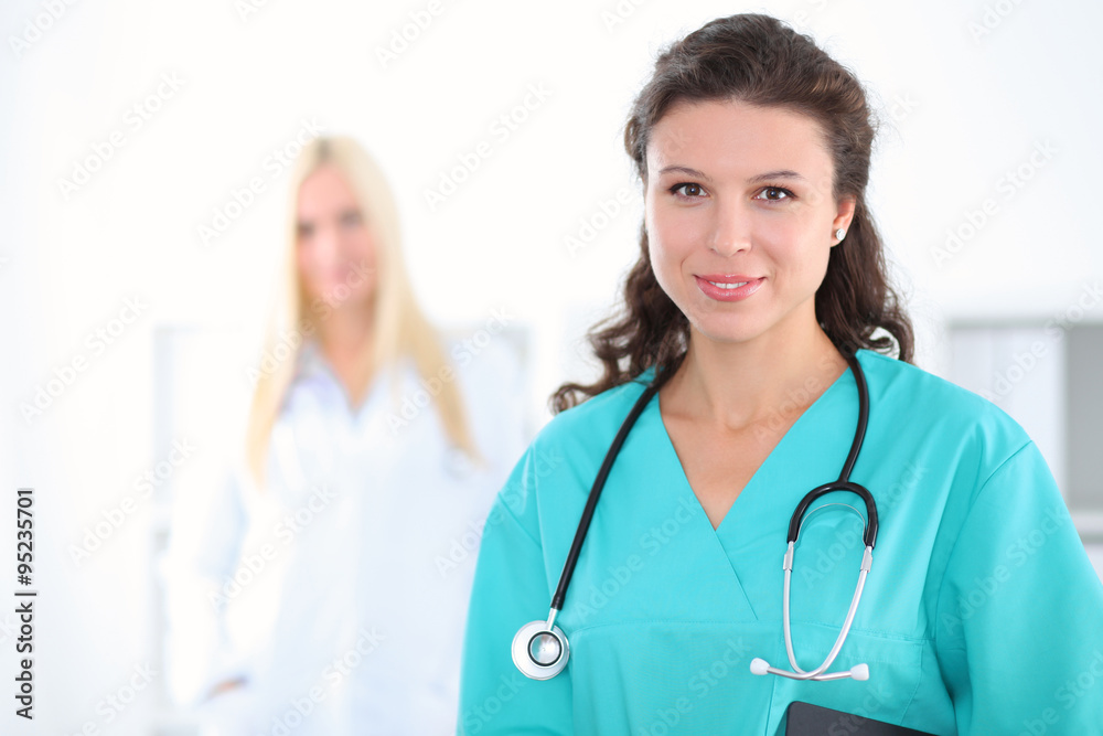 Beautiful young smiling female doctor standing at hospital with doctor on the background. Medical concept. Beautiful young smiling female doctor standing at hospital with doctor on the background. Medical concept.