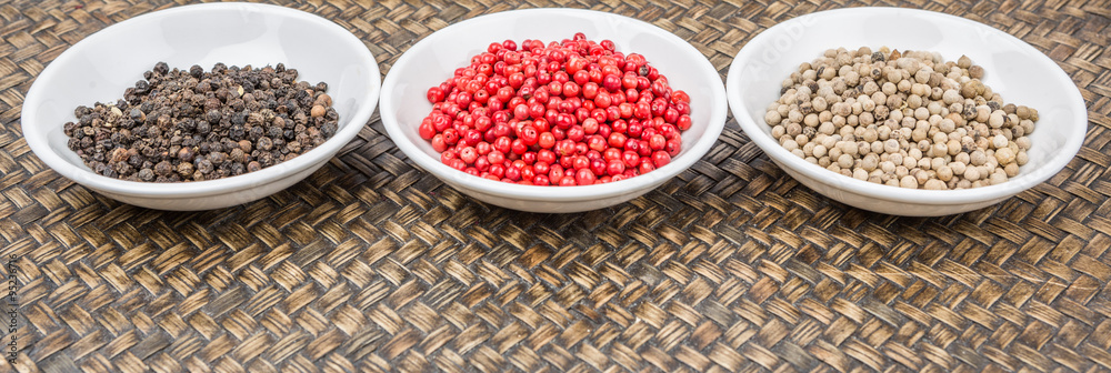 Black, white and pink peppercorn in white bowl over wicker background