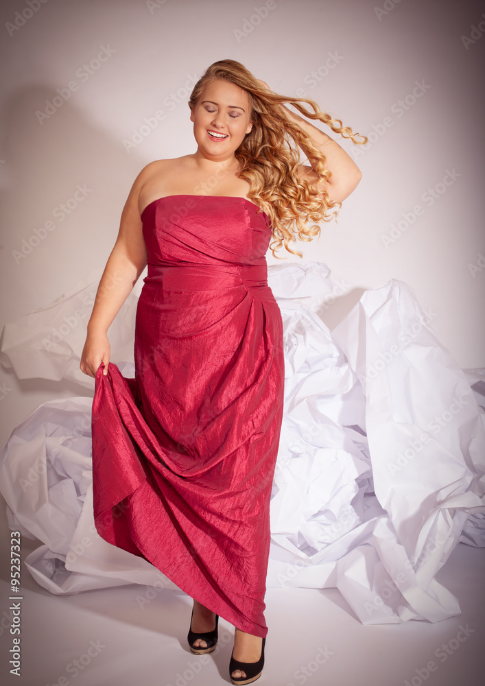 Porträt einer blonden lockigen Frau mit großen Brüsten, in einem roten Abendkleid lachend mit