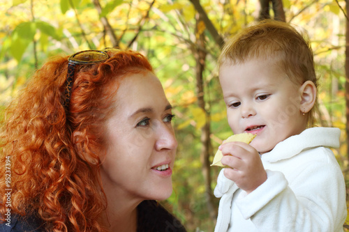 Young mother talks with her little daughter with yellow leaf 