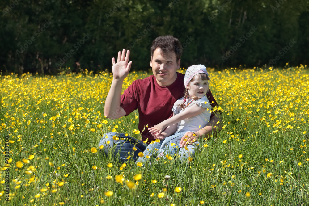 Fototapeta premium Young man with little daughter among yellow flowers at meadow 