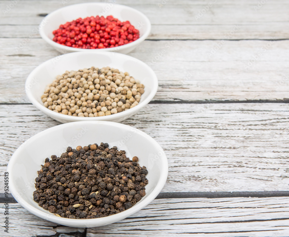 Black, white and pink peppercorn in white bowl over wooden background Black, white and pink peppercorn in white bowl over wooden background