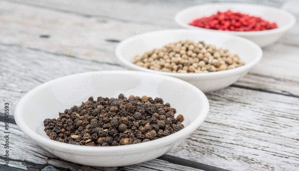 Black, white and pink peppercorn in white bowl over wooden background Black, white and pink peppercorn in white bowl over wooden background