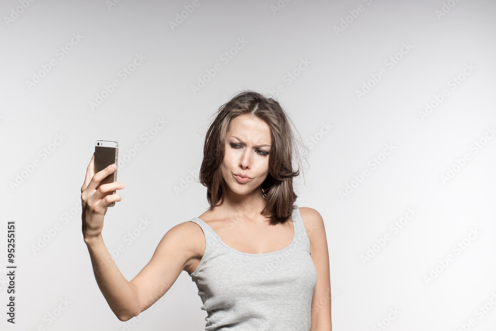 attractive female model is grimacing, making selfies, grey shirt and jeans, white background attractive female model is grimacing, making selfies, grey shirt and jeans, white background