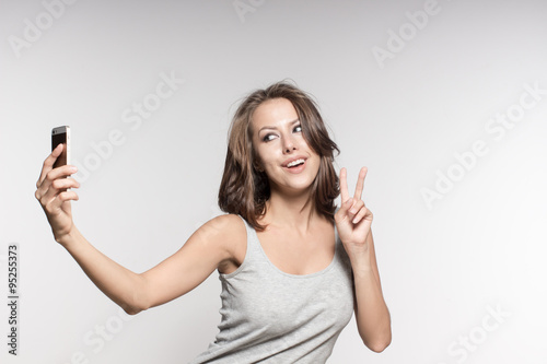 attractive female model is grimacing, making selfies, grey shirt and jeans, white background