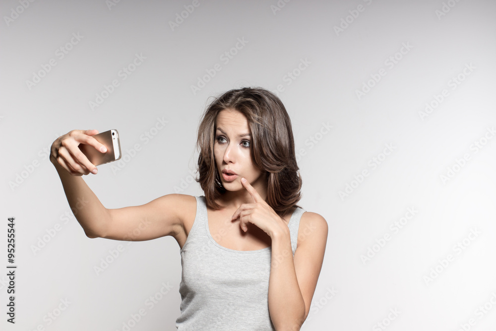attractive female model is grimacing, making selfies, grey shirt and jeans, white background attractive female model is grimacing, making selfies, grey shirt and jeans, white background