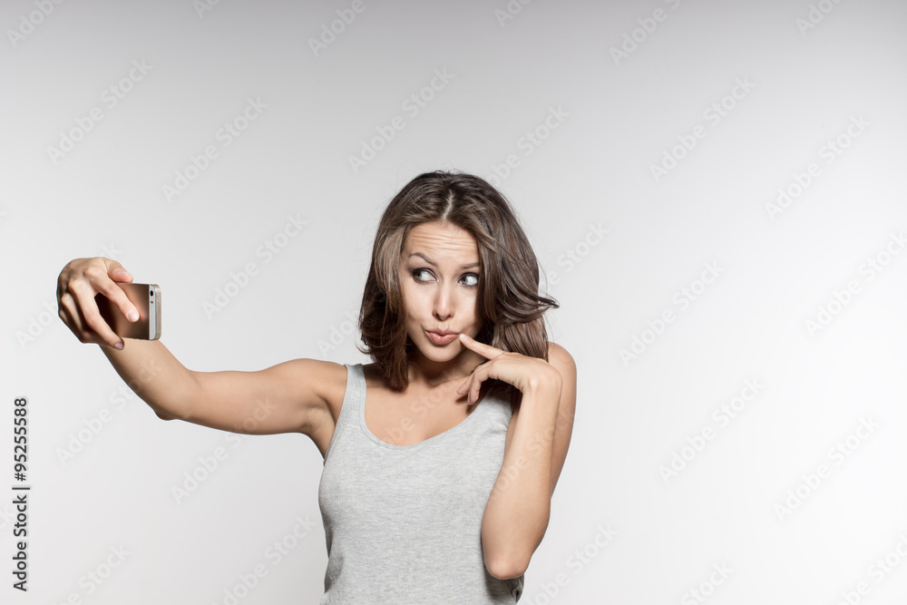 attractive female model is grimacing, making selfies, grey shirt and jeans, white background attractive female model is grimacing, making selfies, grey shirt and jeans, white background