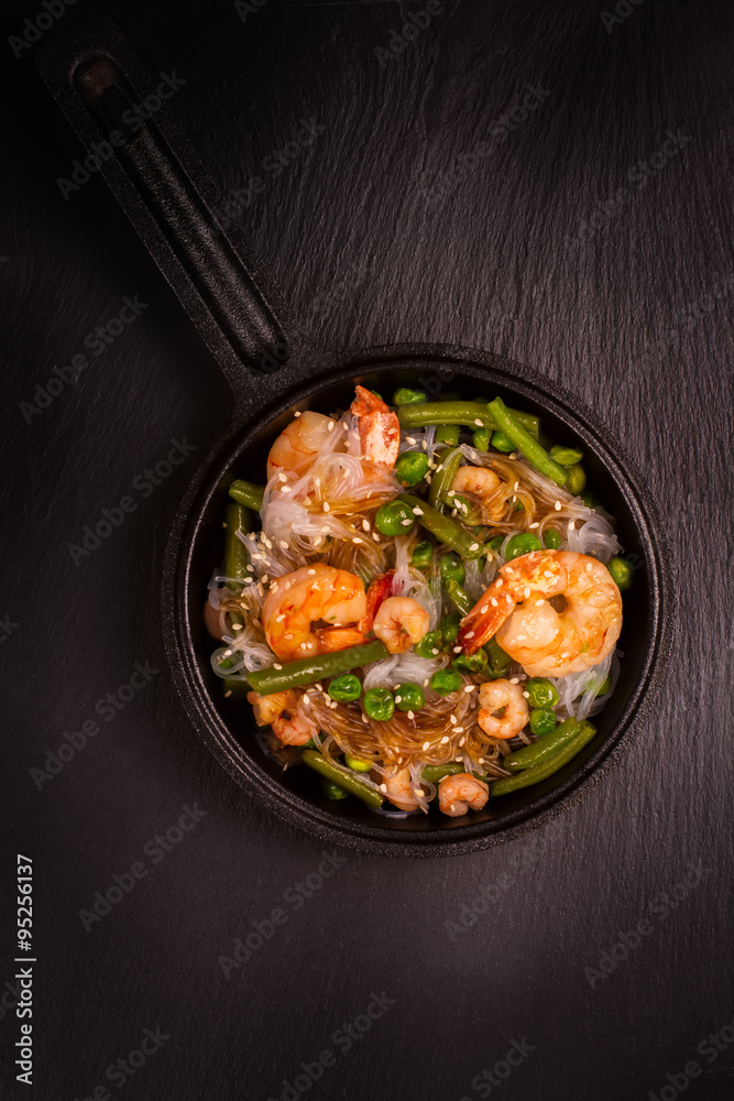 Glass noodle with shrimps and green vegetables in cast-iron pan. Healthy food concept. Top view. Toned image Glass noodle with shrimps and green vegetables in cast-iron pan. Healthy food concept. Top view. Toned image