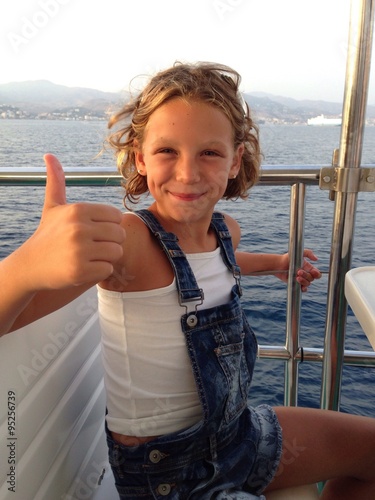 niña rubia sonriente navegando en un barco de recreo levantando el pulgar photo